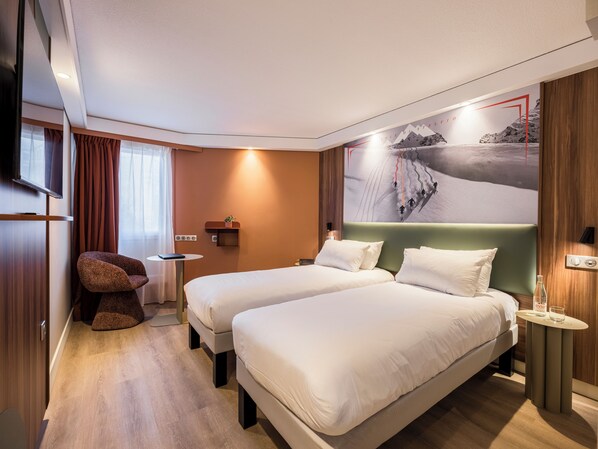 A hotel room with two beds, a TV, a small table, a chair, and a wall-mounted shelf.