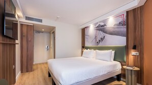 A modern hotel room with a large bed, a television, and a wall-mounted artwork. - ibis Styles Annecy Le Vieux (Annecy)