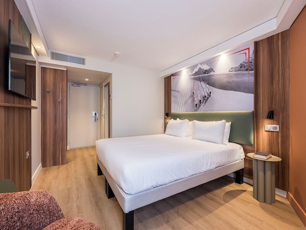 A modern hotel room with a large bed, a television, and a wall-mounted artwork.