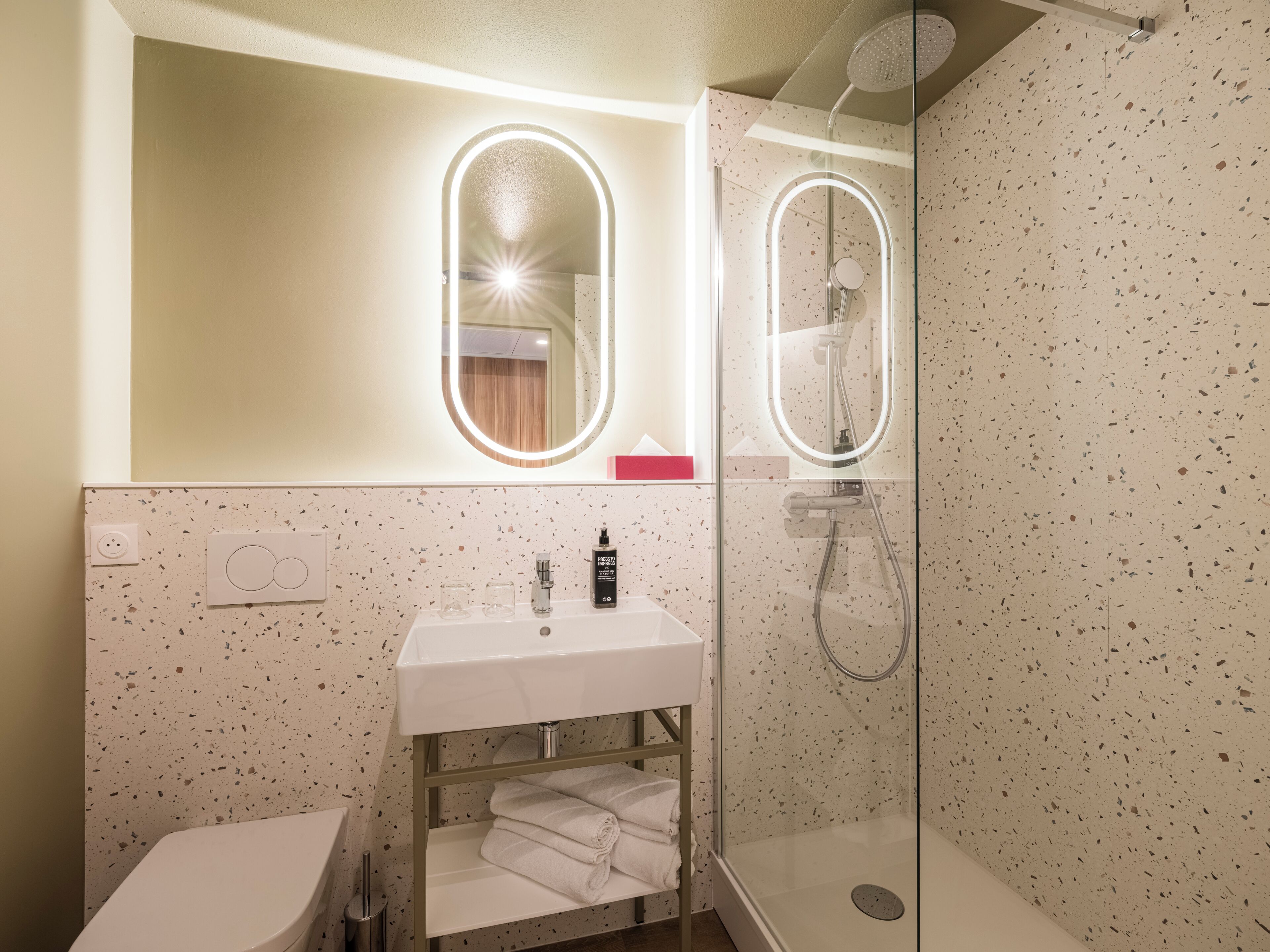 Un baño con un lavabo blanco, ducha con cerramiento de cristal y espejo con iluminación.
