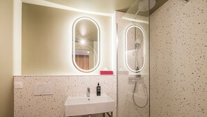 Un baño con un lavabo blanco, ducha con cerramiento de cristal y espejo con iluminación.