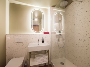 A bathroom with a white sink, a glass-enclosed shower, and a mirror with lights.