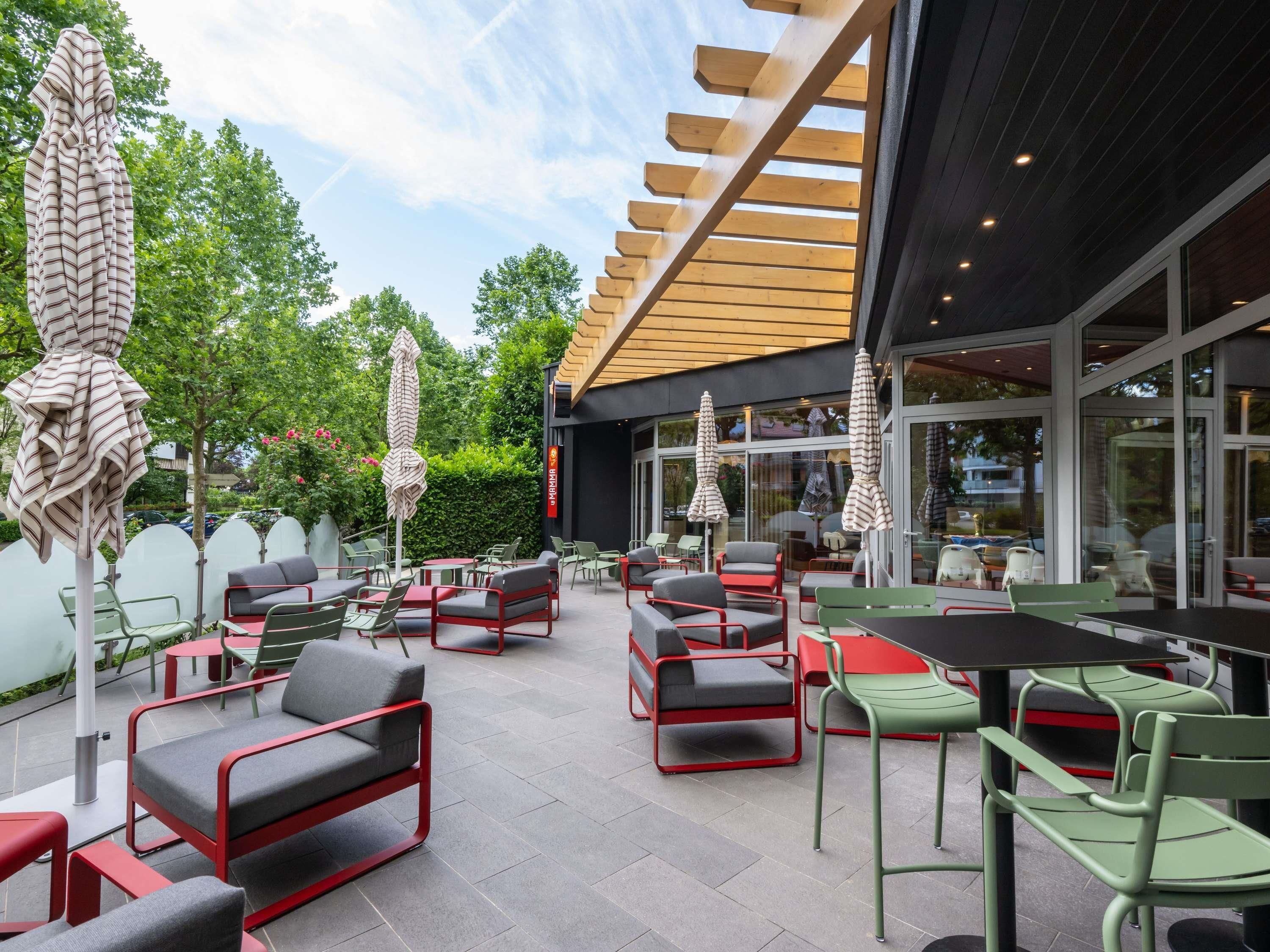 An outdoor seating area with tables and chairs, umbrellas, and a wooden pergola structure.