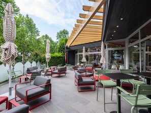 Un área de estar al aire libre con mesas, sillas, sombrillas y una estructura de pérgola de madera.