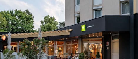 Un hotel con fachada moderna, entrada visible con escalones y asientos al aire libre.