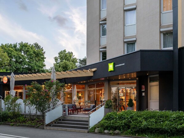 Un hotel con fachada moderna, entrada visible con escalones y asientos al aire libre.
