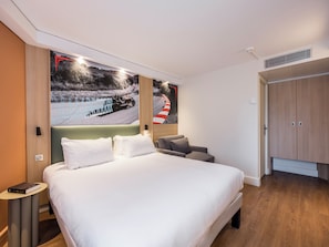 A hotel room with a large bed, a bedside table, a chair, and a wardrobe.