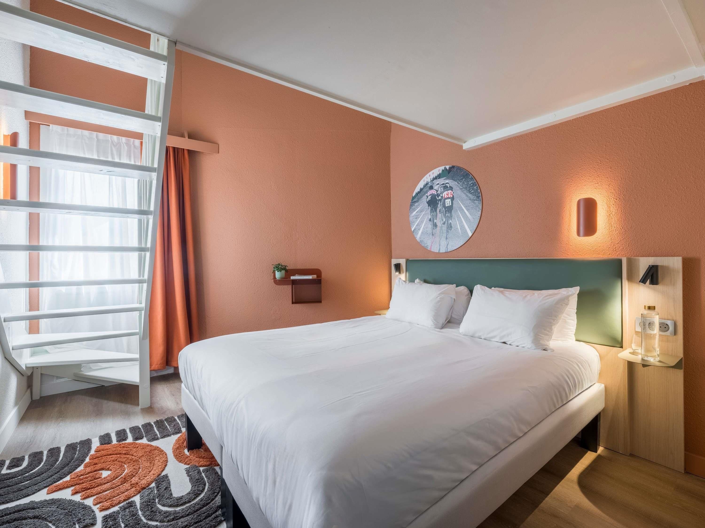 A hotel room with a bed, a wall-mounted light, a circular artwork, and a window with curtains.