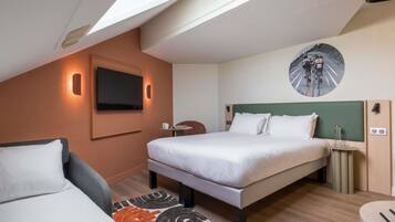 Hotelkamer met een bed, een aan de muur bevestigde televisie, een klein tafeltje met een lamp en een rond kunstwerk aan de wand.
