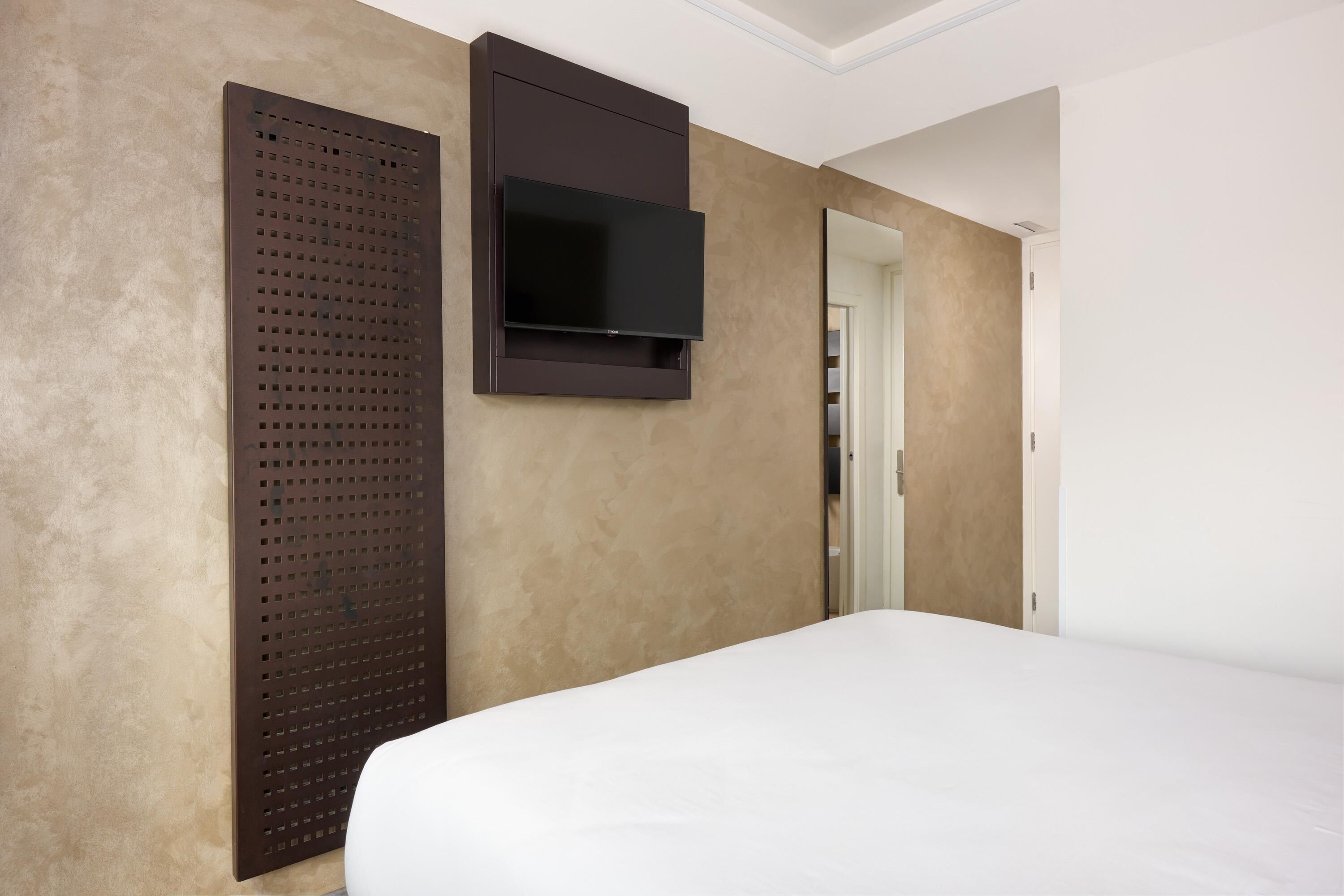 A hotel room with a bed, a wall-mounted TV, and a door leading to a closet.