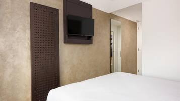 A hotel room with a bed, a wall-mounted TV, and a door leading to a closet.