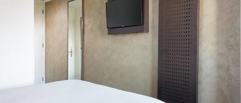 A modern hotel room with a bed, a flat-screen TV mounted on the wall, and a large window.