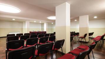 Ein Konferenzraum mit Reihen schwarzer Stühle mit roten Kissen, einer Whiteboard-Tafel und einem Tisch mit roter Tischdecke.