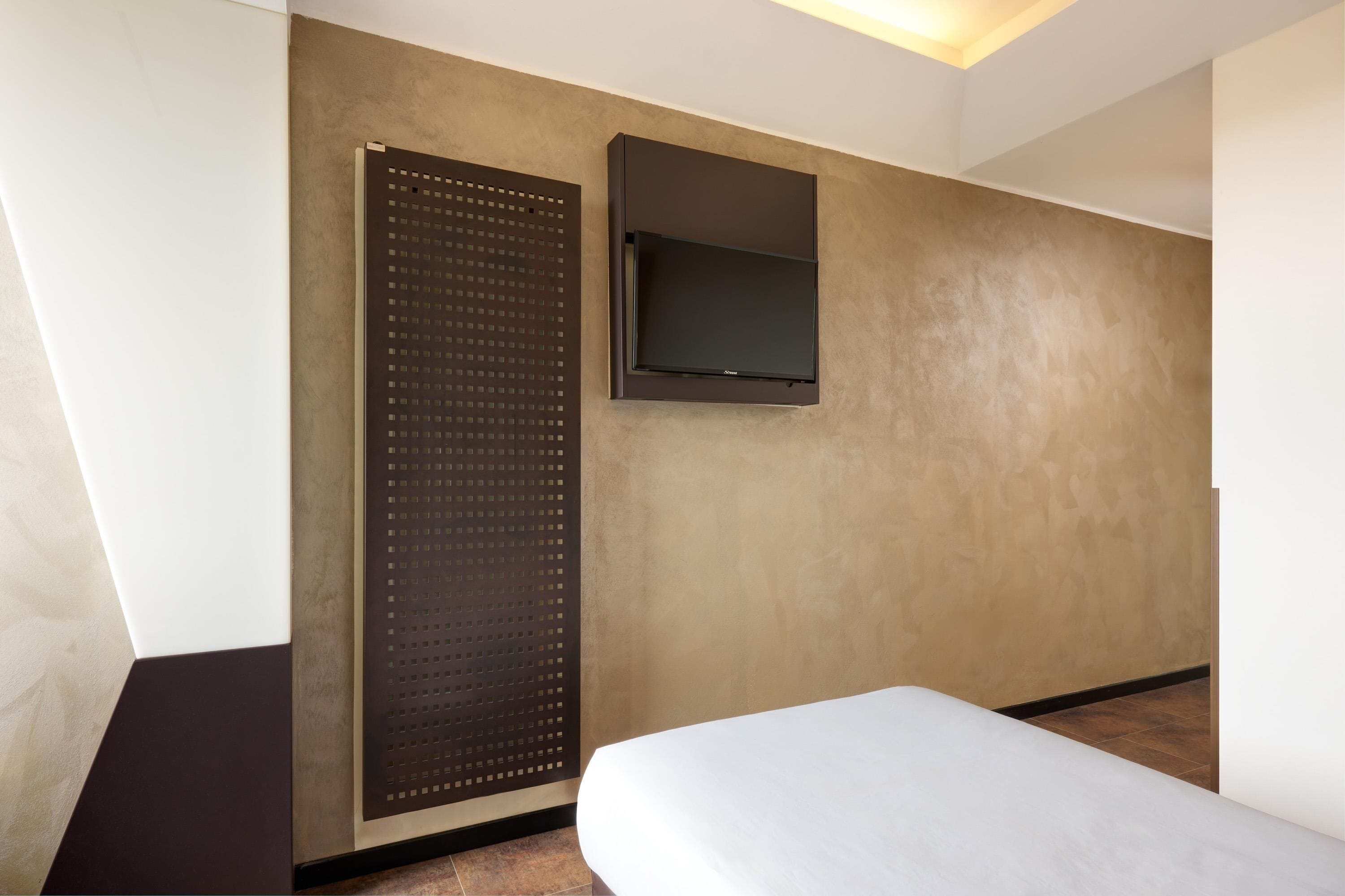 A hotel room with a bed, a wall-mounted TV, and a large window.