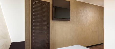 A hotel room with a bed, a wall-mounted TV, and a large window.