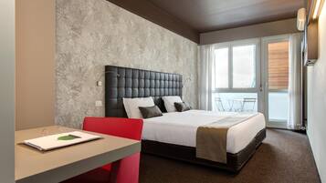 Ein Hotelzimmer mit Bett, Schreibtisch mit Stuhl, Fenster mit Jalousien und einer Tür.