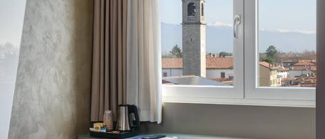 A hotel room with a desk, a red chair, a window with a view of a tower and mountains.