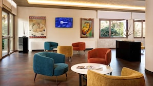 A spacious lobby with modern furniture, artwork on the walls, and large windows offering views of greenery.
