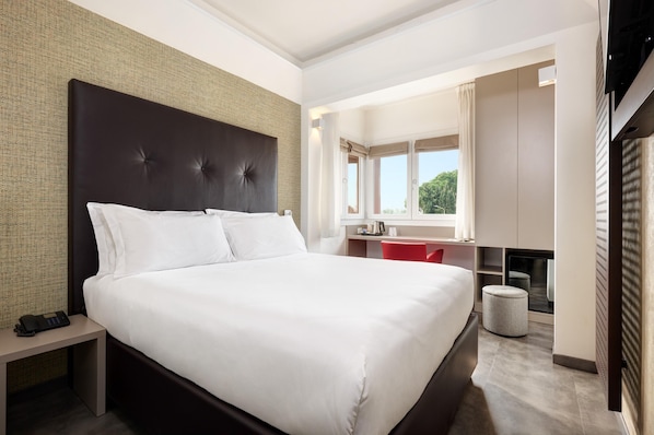 Une chambre d’hôtel moderne avec un grand lit, un bureau, une chaise et un petit pouf.