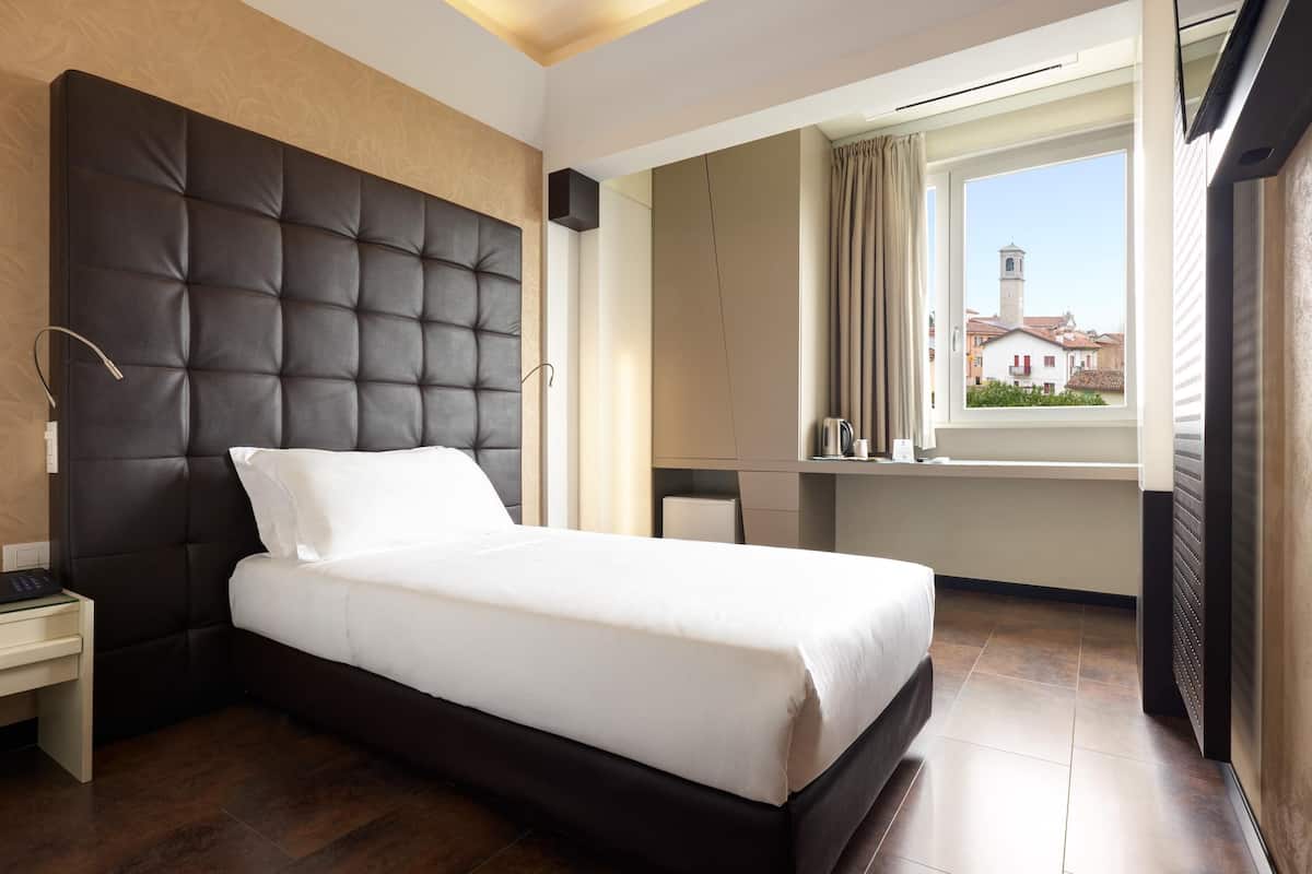 Camera d'albergo moderna con un ampio letto, una scrivania, una finestra vista edifici e un armadio.