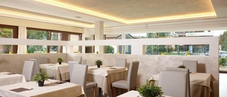 Un restaurante moderno con mesas cubiertas de manteles color beige, sillas y plantas en macetas.
