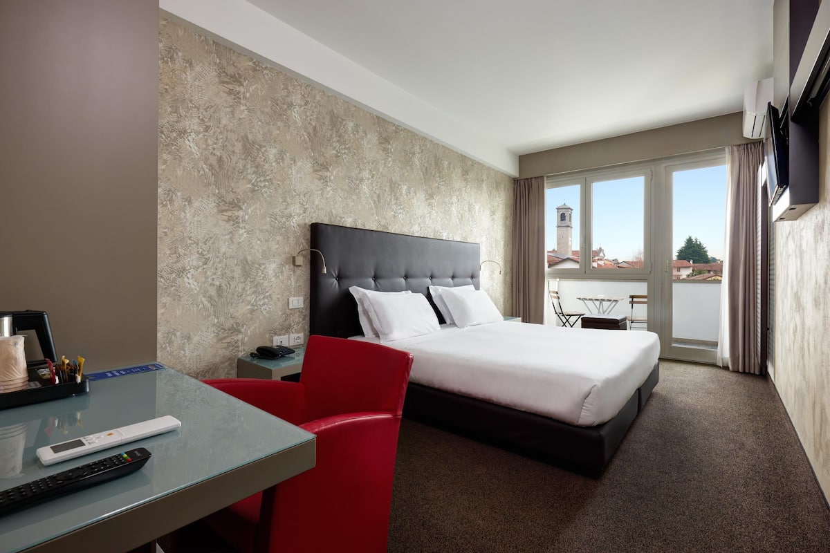 Camera d'albergo con un letto, una scrivania con sedia, televisione e vista sugli edifici.