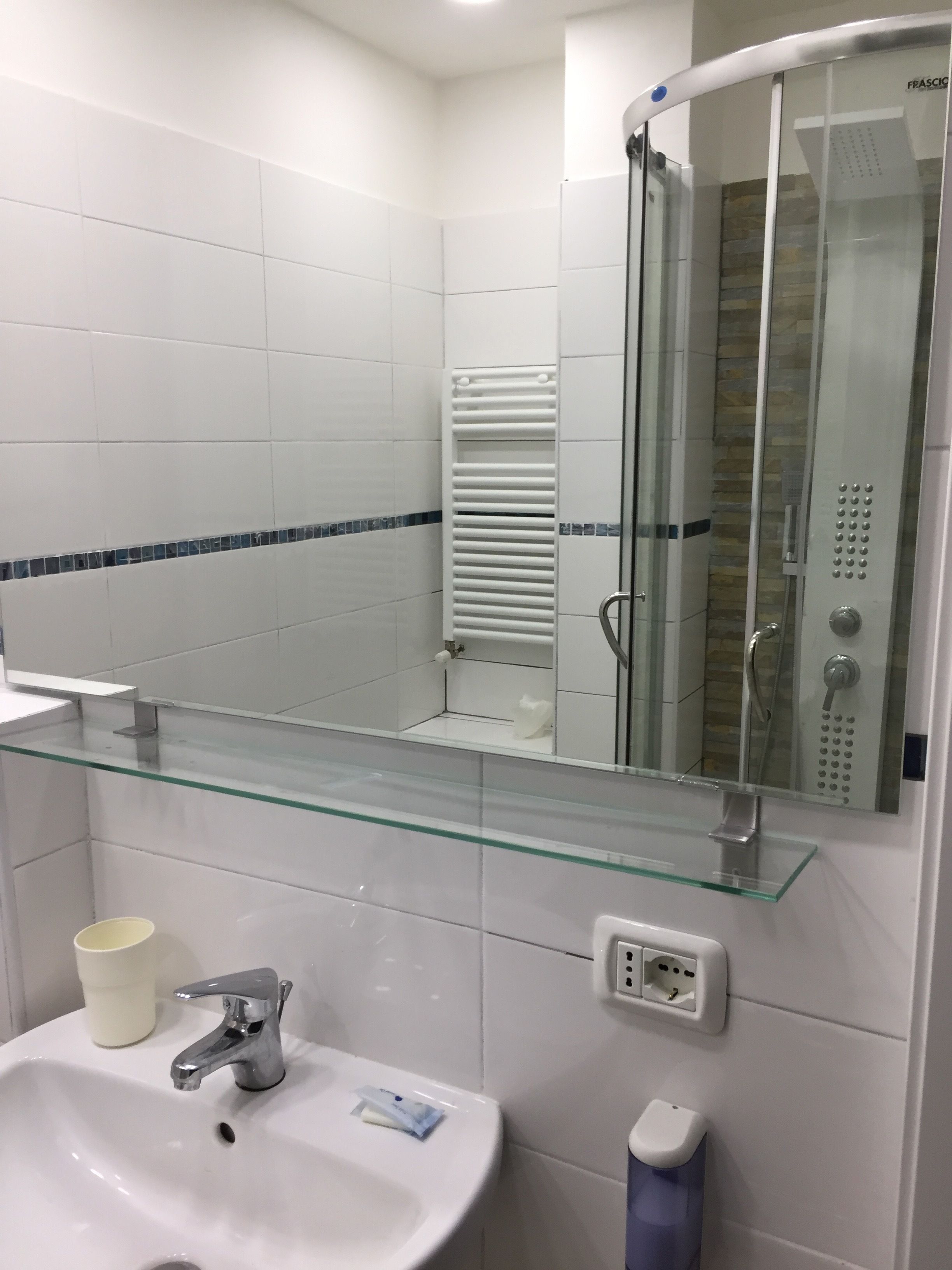 Un baño moderno con cabina de ducha de vidrio, un lavabo blanco con espejo y un estante de vidrio.