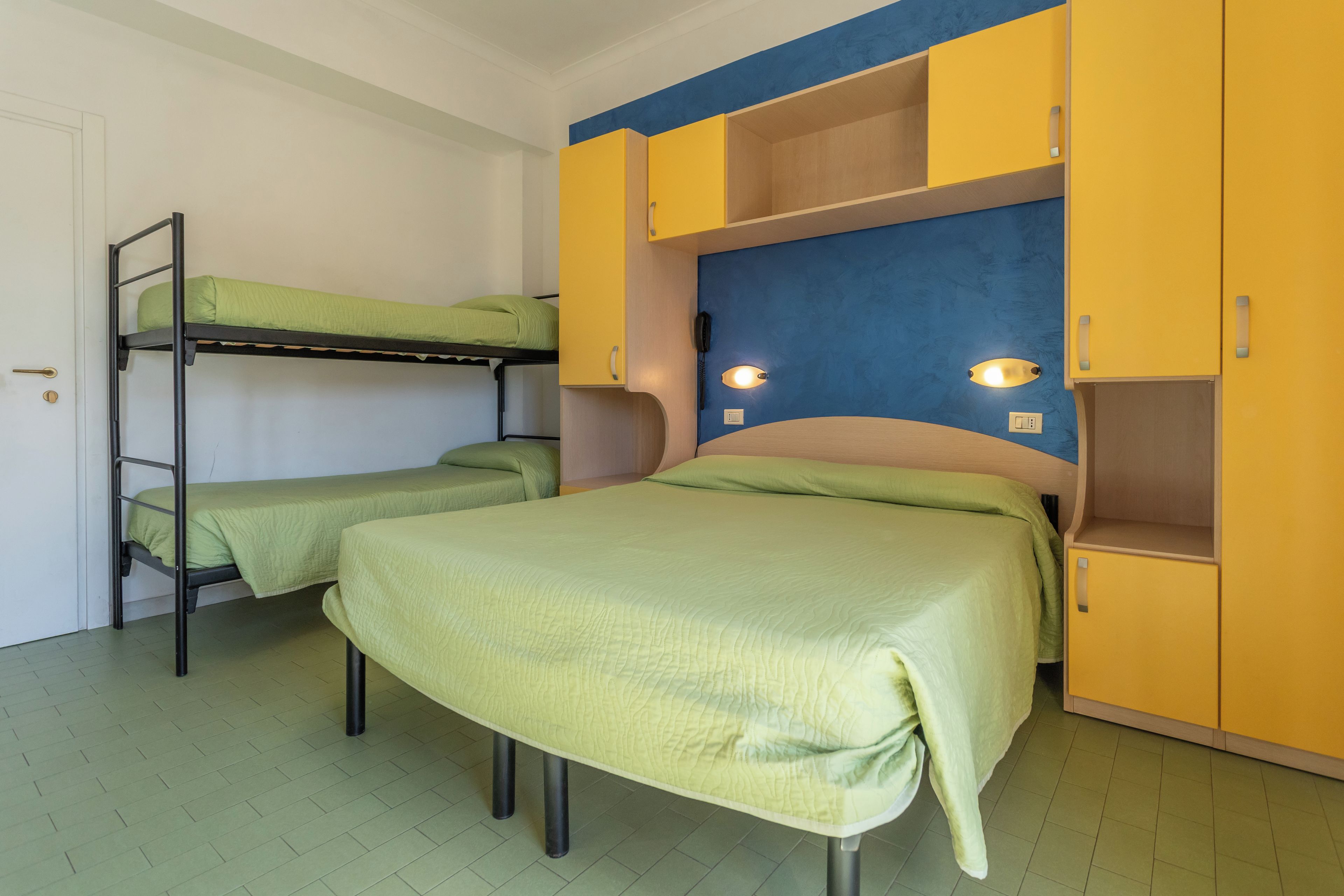 A room with bunk beds, a desk, and a bed with a headboard.
