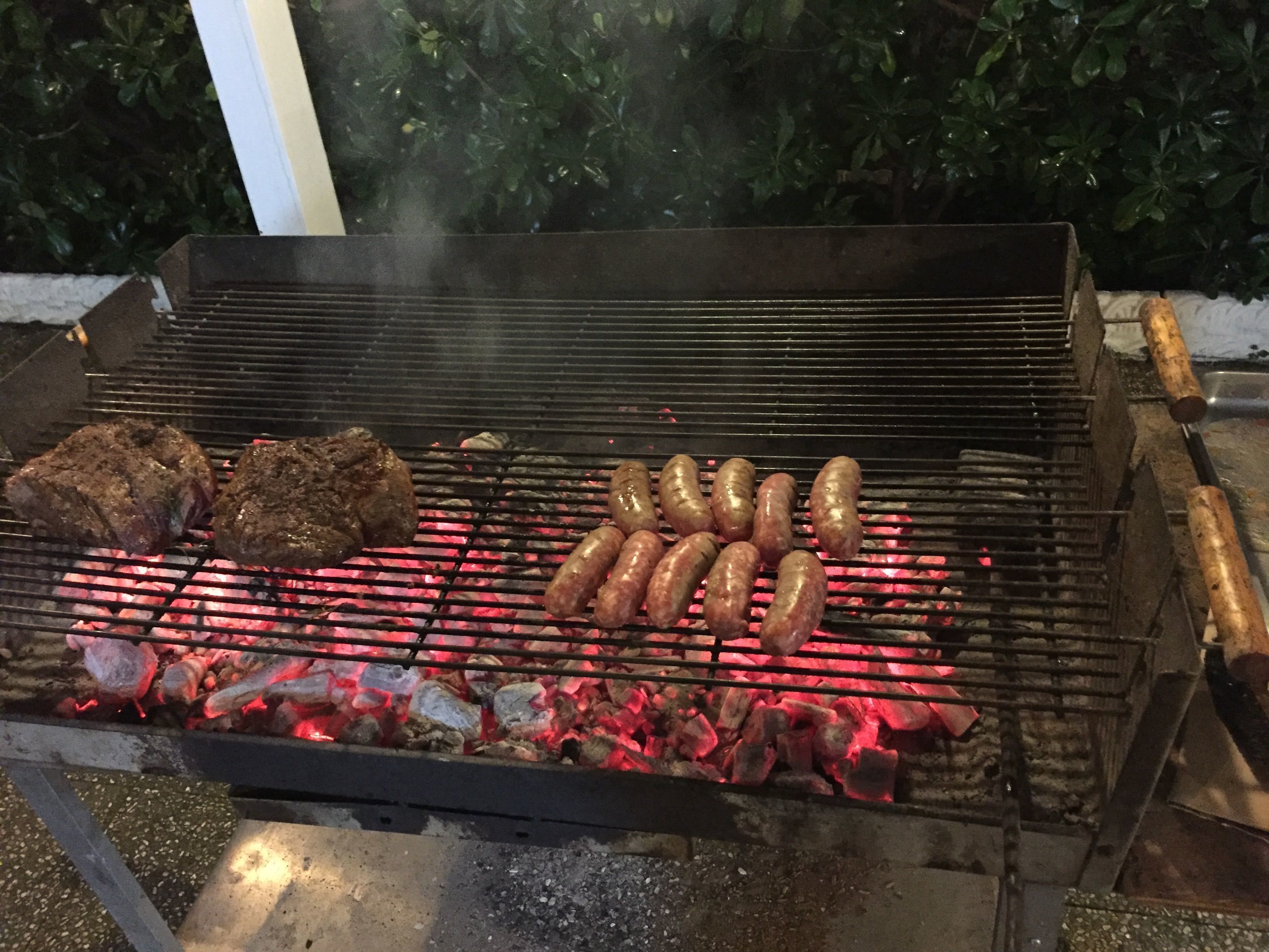 A barbecue grill with meat and sausages being cooked.