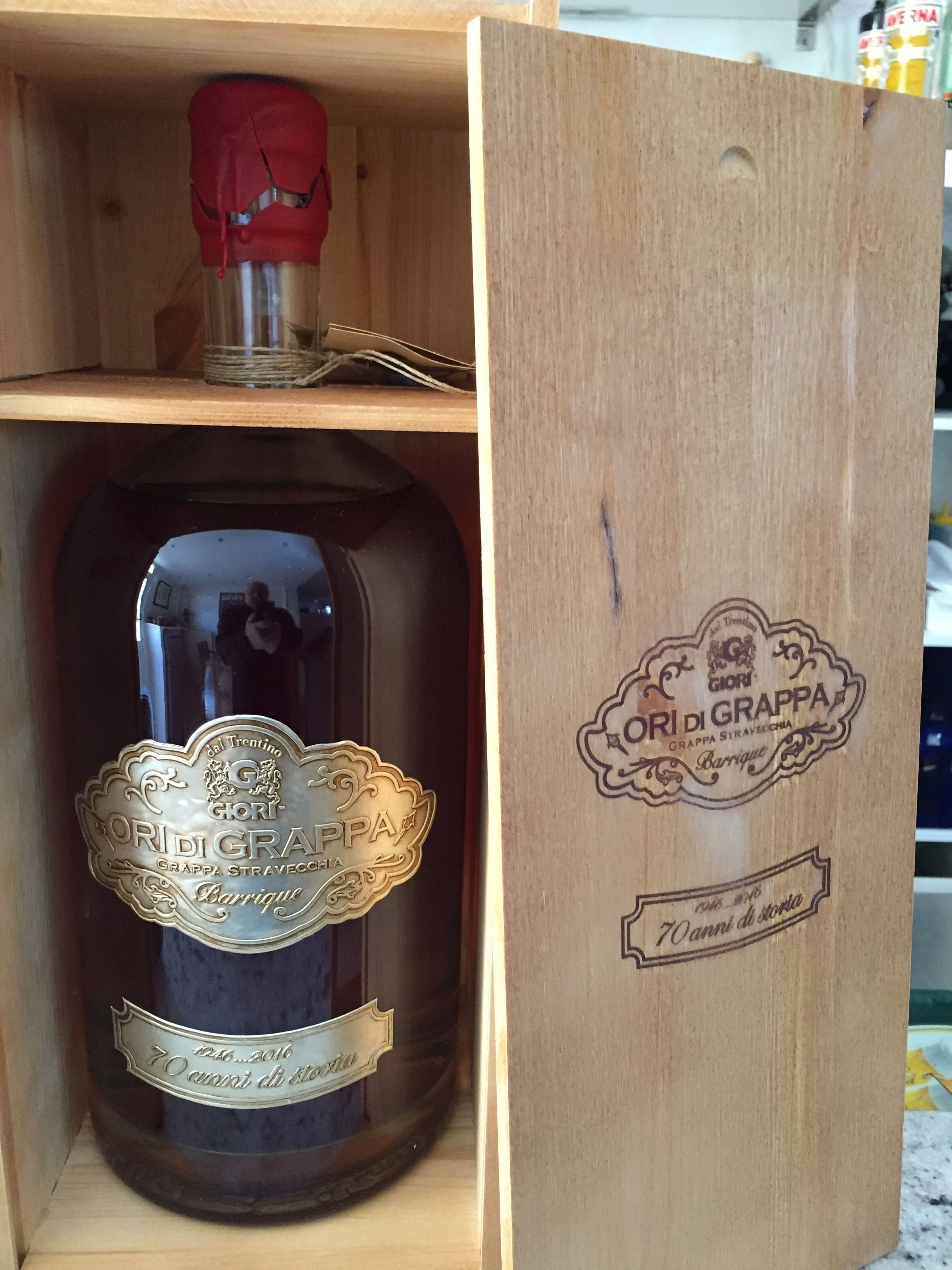A wooden box containing a bottle of wine with a label that reads "ORIGI DI GRAPPA" and "70 anni di storia".