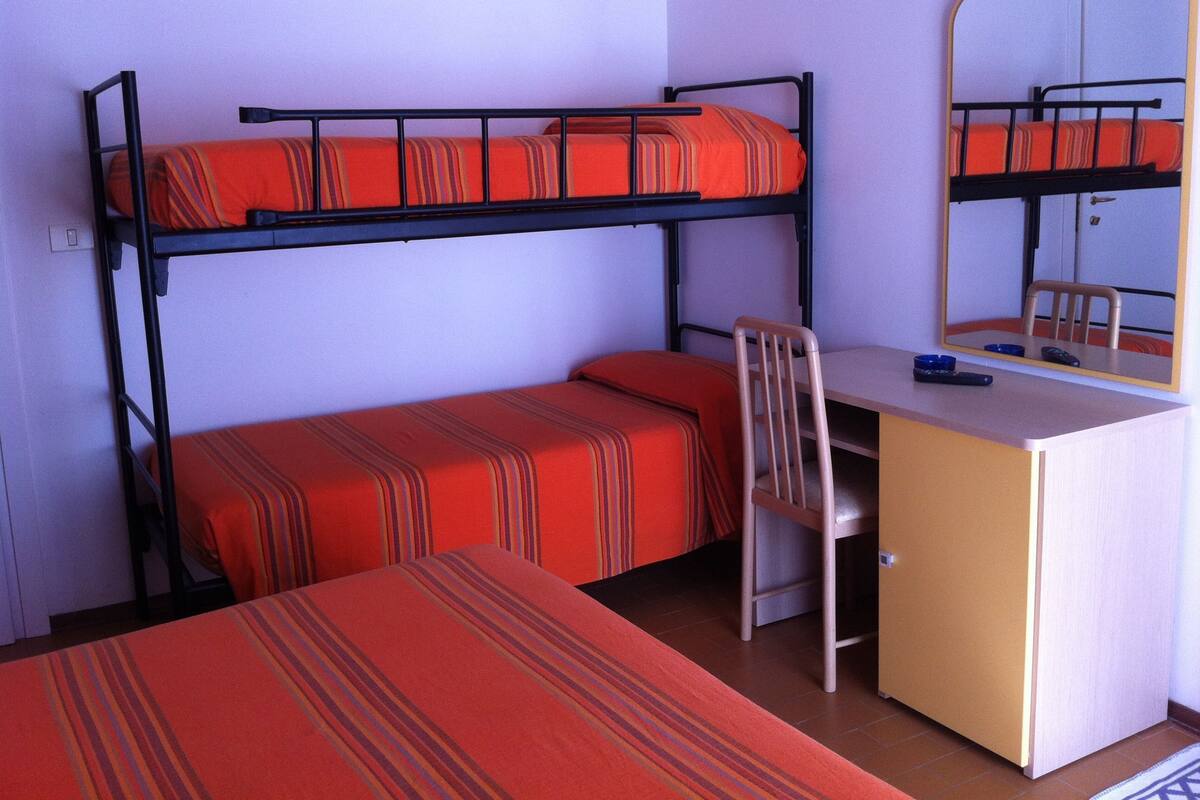 A bunk bed with a desk and chair, a mirror, and a small table with a remote control.