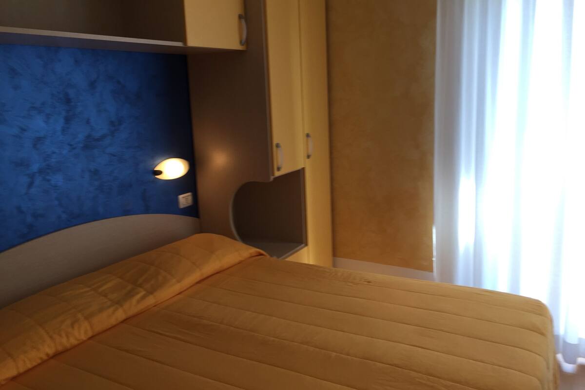 A room with a bed, a blue wall, a light fixture, and a window with curtains.