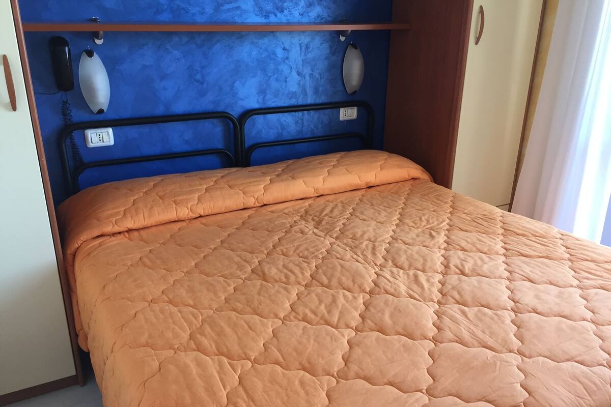 A bedroom with a blue headboard, a bed with an orange quilt, and a bedside telephone.