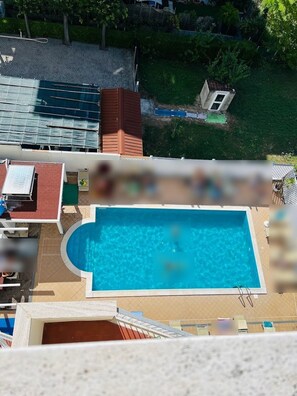 A swimming pool with a fenced deck area, surrounded by a residential setting with a small building and greenery. - Hotel Viking (Rimini)
