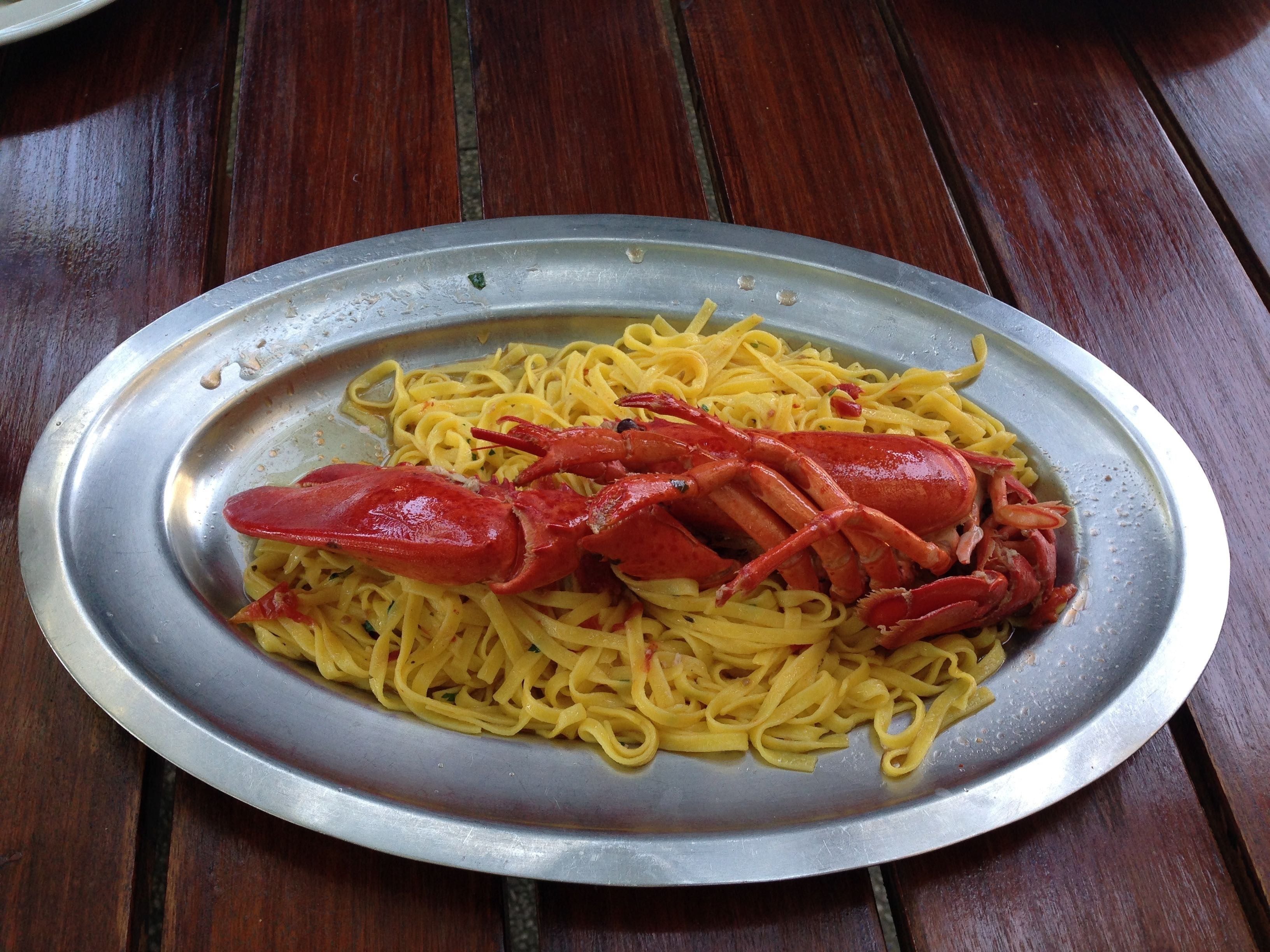 A plate of spaghetti with a lobster on a metal tray.