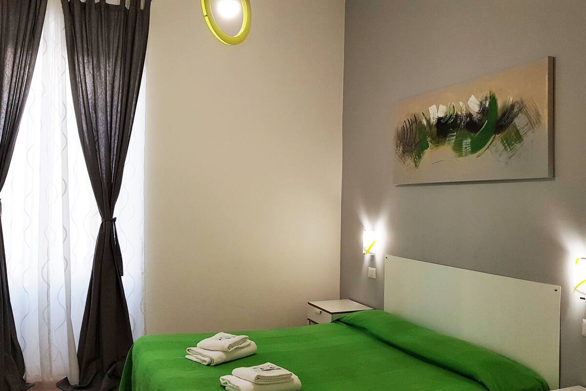 A hotel room with a bed, a painting on the wall, and a nightstand with a lamp.