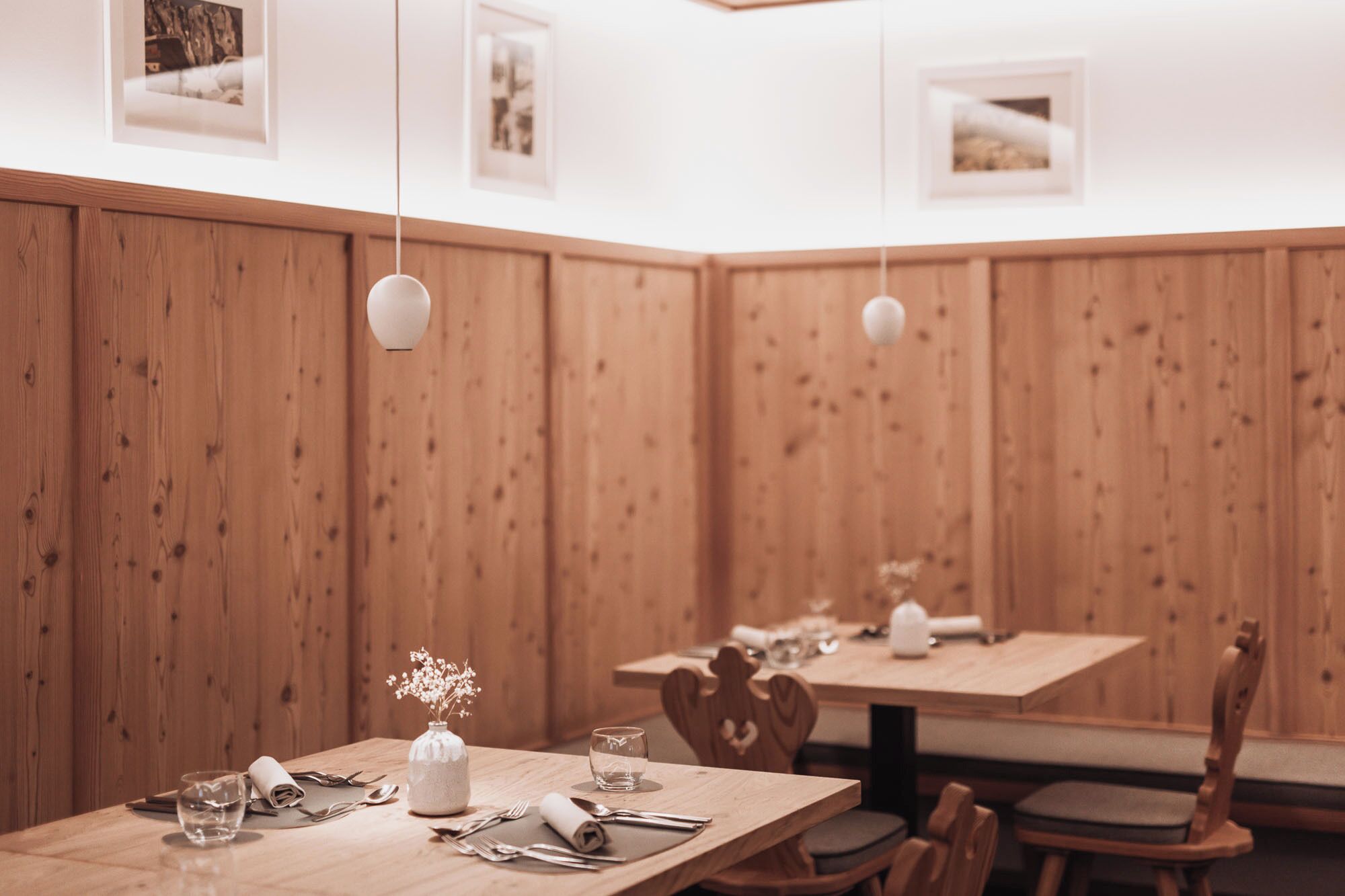 A restaurant with wooden panel walls, tables set with cutlery, glasses, and a vase with flowers.