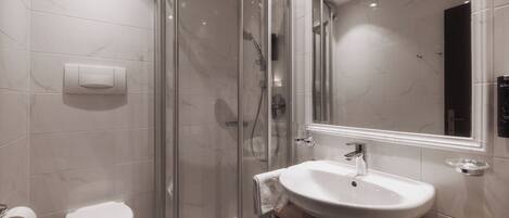 Un baño moderno con ducha envuelta en vidrio, un lavamanos blanco y un inodoro.