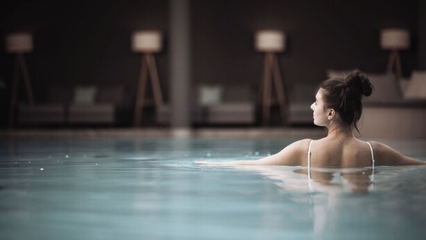 A person in a swimming pool with lounge chairs and tables in the background. - Hotel Montis - Schönblick (Brunico)