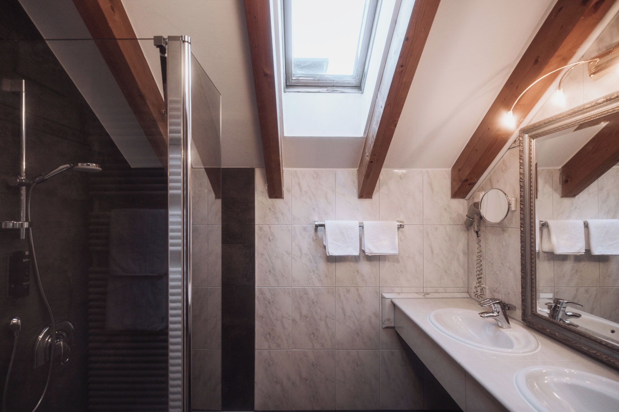 Un baño moderno con tragaluz, ducha y dos lavamanos.