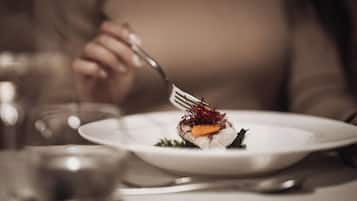 A person dining at a table with a white plate containing a dish, a fork, and a glass of water.