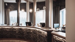 A modern reception area with stone walls, a curved reception desk, and multiple computer stations. - Hotel Montis - Schönblick (Brunico)