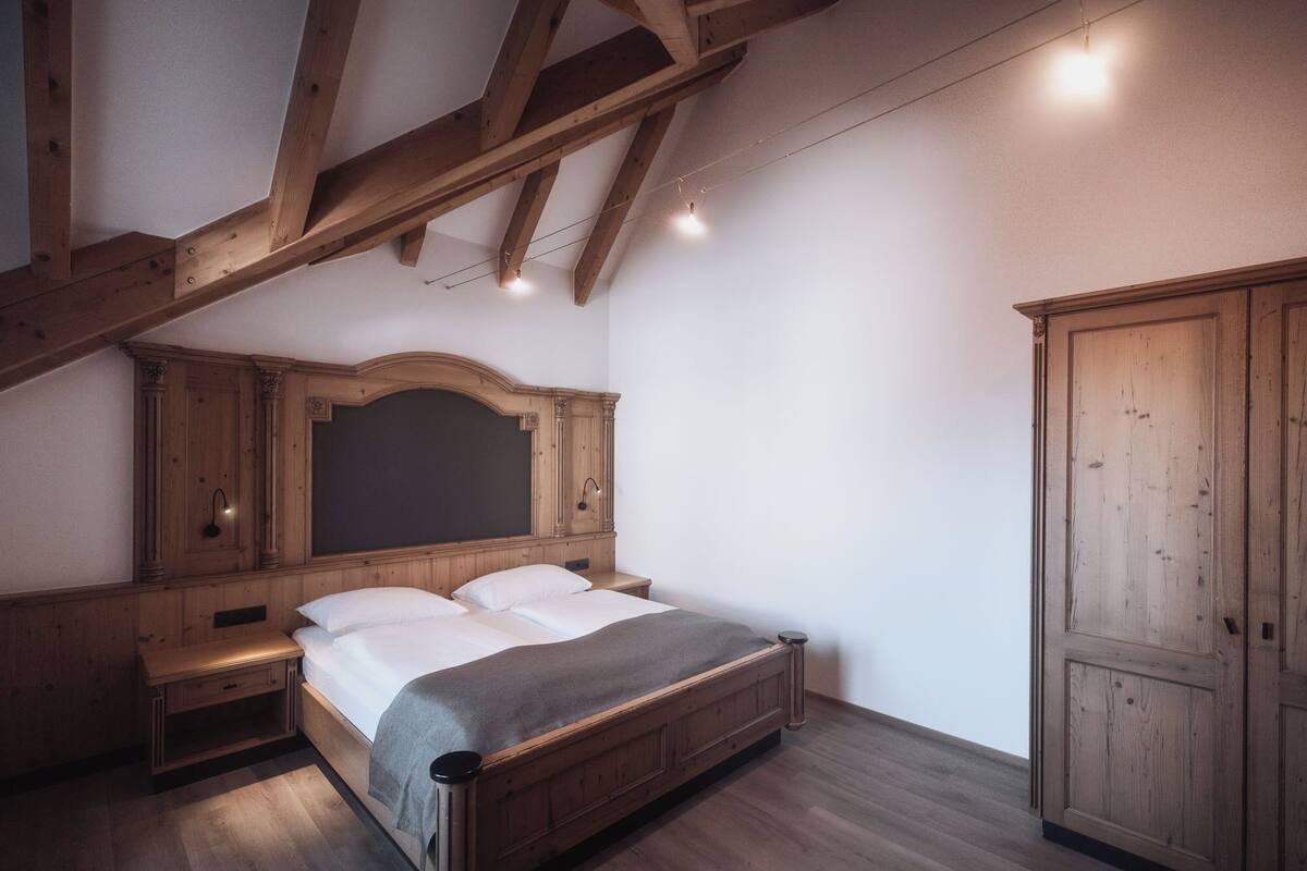 Une chambre avec un lit en bois, une table de chevet, une armoire et des poutres apparentes en bois au plafond.