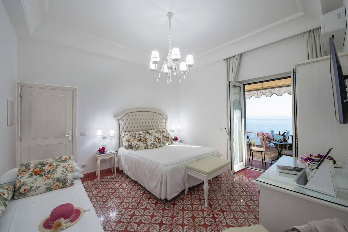 A bedroom with a bed, bedside table, and a view of the sea.