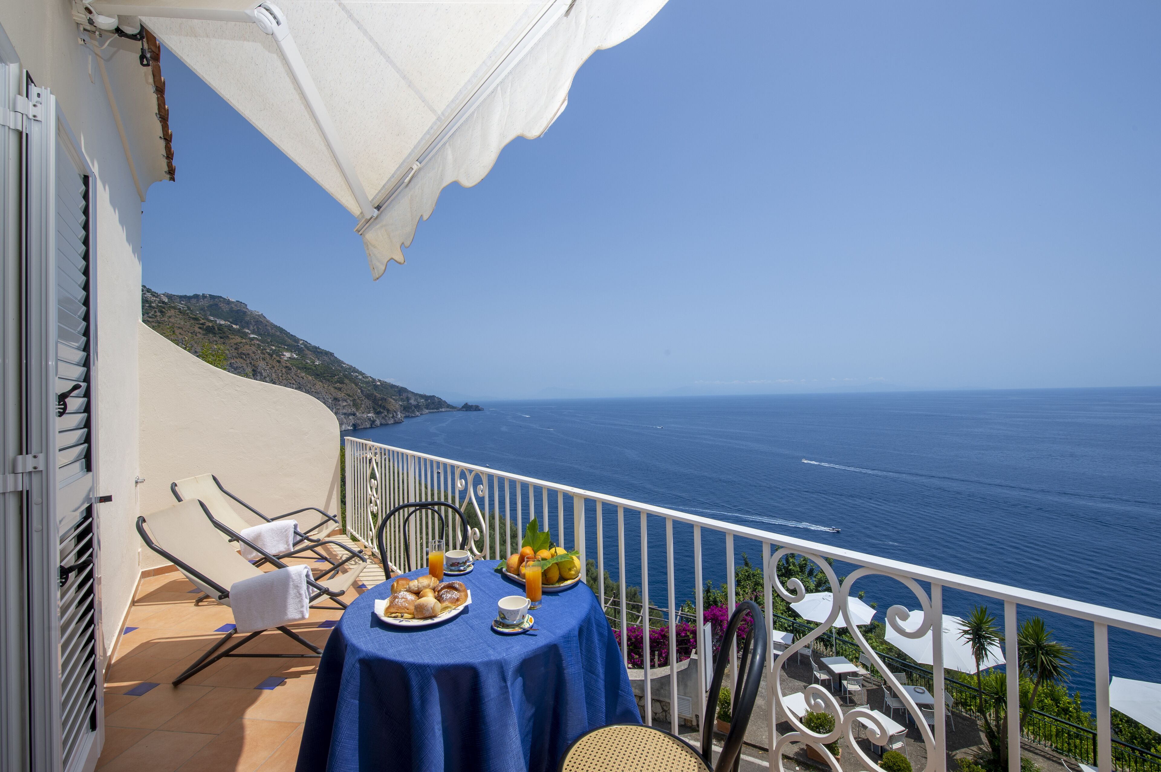 A balcony with a table set for breakfast, overlooking the sea.