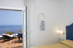 A balcony with a view of the sea, a dining table with chairs, and a bed with a blue headboard.