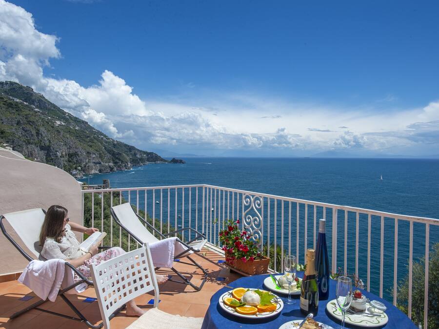 A balcony with a table set for two, overlooking a coastal view.