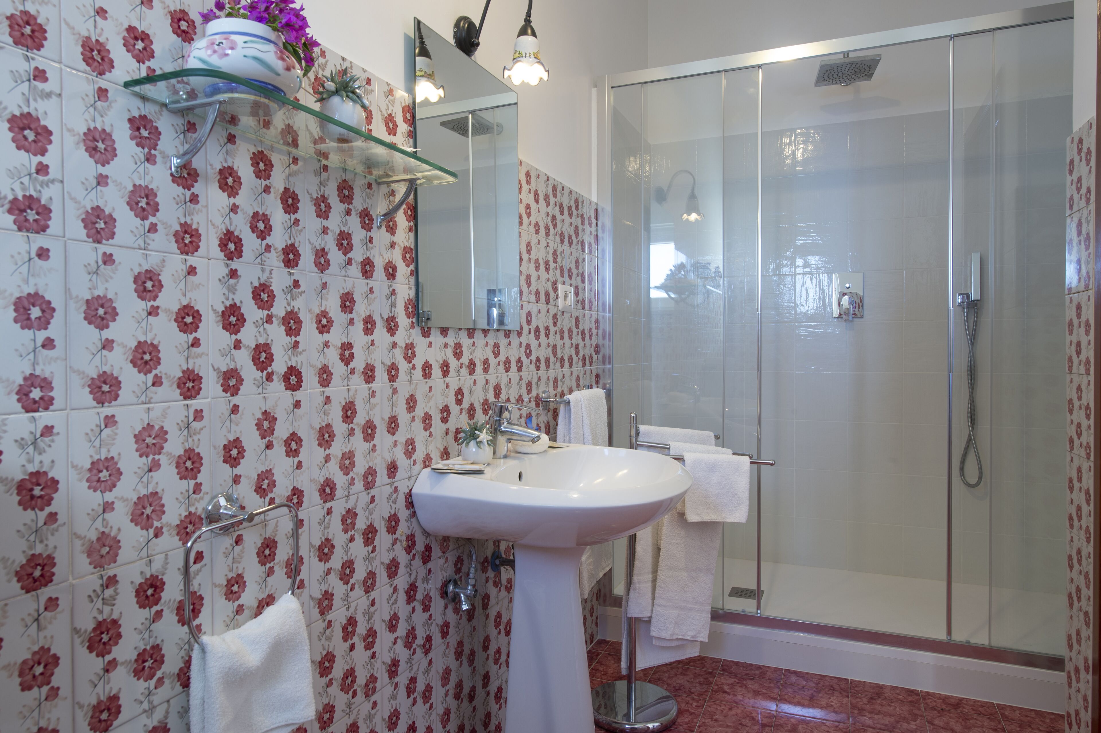 A bathroom with a white sink, a glass shower enclosure, and floral-patterned tiles.