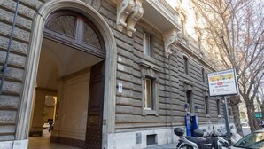 A historic building with a large arched entrance, a sign for a bus shuttle service, and a parked scooter on the sidewalk. - Marta Guest House (Rome)