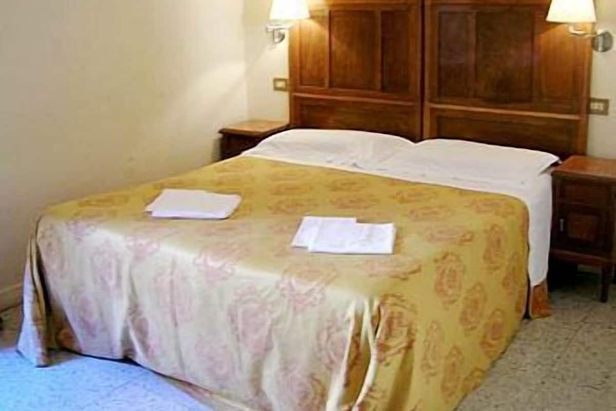 A hotel room with a wooden headboard, two bedside lamps, a bed with a floral bedspread, and a nightstand with a lamp.